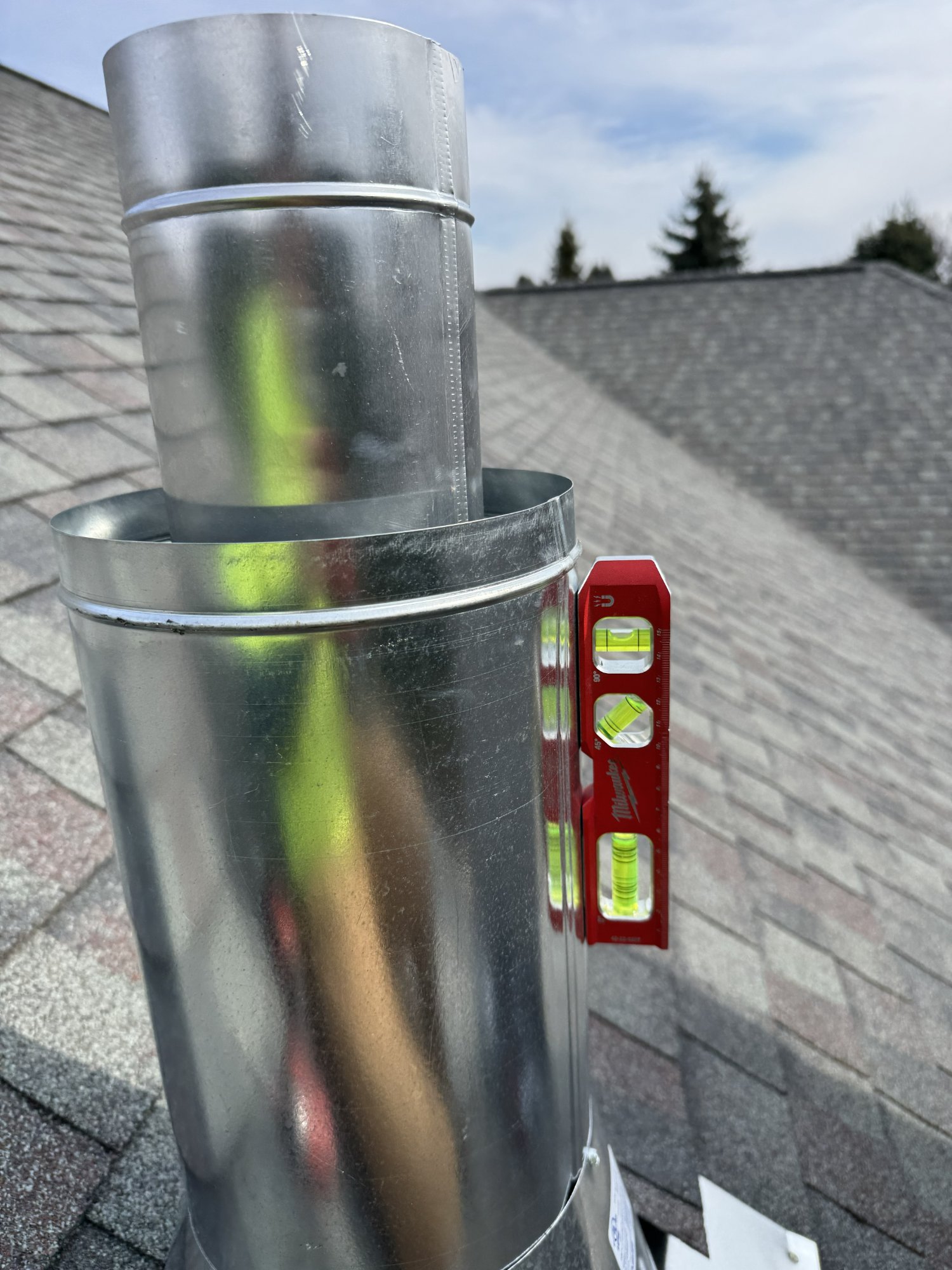 Chimney flue cap installation with level check on asphalt shingle roof